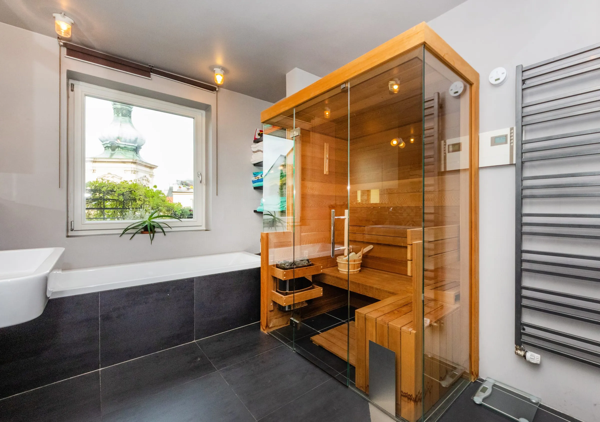 Glass-walled Finnish sauna next to a tub and a window onto a church tower